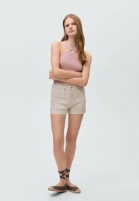 Svetlo rožnata rebrasta majica s posnetkom na sprednjem delu, v kombinaciji s smetanastimi kavbojkami. Rjavi espadrilci z naramnicami dopolnjujejo videz.