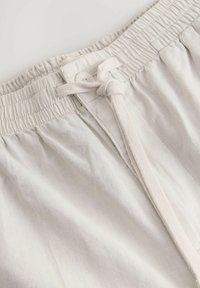 Lichtbeige shorts met een elastische tailleband. Voorzien van een trekkoordsluiting en een knoop. Stof lijkt glad met een lichte textuur.