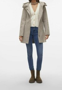 Vaaleanharmaa villasekoitetakki huppulla, yhdistetty kermaiseen palmikkoneulecardiganiin ja sinisiin skinny-farkkuihin, päällä ruskeat nilkkurit.