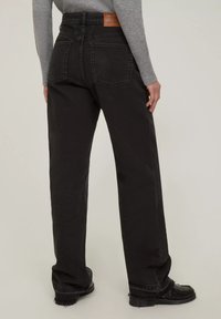 Jeans neri in denim a vita alta con gamba dritta, caratterizzati da tasche posteriori e un'etichetta in pelle in vita. Tessuto testurizzato.