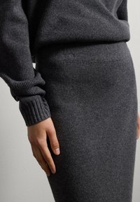 Vestido de punto acanalado en gris oscuro que presenta un silueta ajustada, mangas largas y una textura suave, enfatizando la calidez y comodidad.