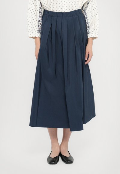 Marineblauer Faltenrock aus leichtem Stoff; hat einen elastischen Bund, ist knöchellang und hat eine glatte Textur. Getragen mit schwarzen Ballerinas.