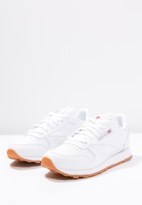 Witte sportieve schoenen met leren bovenzijde, contrasterende gumrubberen zool, geperforeerde details en branding aan de zijkant en op de tong.