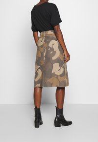 Camo-patterned midi skirt in shades of brown and beige, featuring a high waist, side pocket, and paired with black ankle boots.
