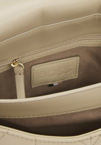 Beżowa skórzana torebka od środka z złotymi elementami, metką marki i gładką fakturą. Posiada kieszeń na zamek oraz przeszycia.
