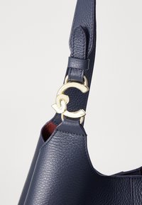 Navy leather handbag featuring a gold metal hardware accent and textured finish, with a secure shoulder strap attachment.