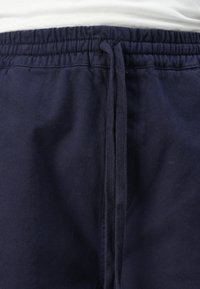 Pantalones de chándal azul marino con cordón, fabricados con un tejido texturizado, con cintura elástica y lazos ajustables. Vista en primer plano de la cintura y la textura del tejido.