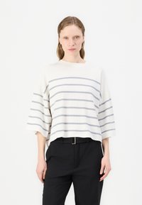 Pulover cu dungi crem, cu linii orizontale gri deschis, având o croială lejeră, mâneci largi și o textură ribbed. Este purtat cu pantaloni negri.