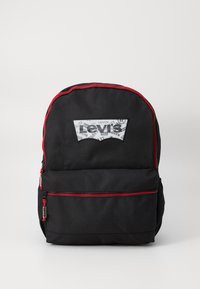 Fekete hátizsák piros cipzár díszítéssel, elülső zsebbel és átlátszó logóval, amely a Levi's márkát ábrázolja. Simább anyagú textúra.