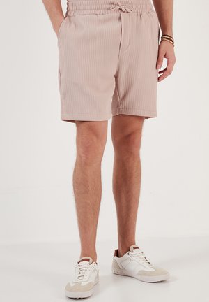 Light pink ribbed shorts with an elastic waistband and drawstring, featuring side pockets and a relaxed fit. Worn with white sneakers.