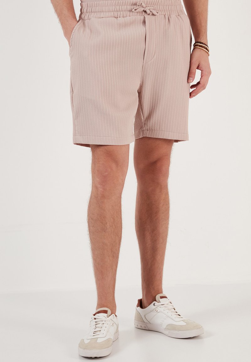 Lichtroze geribde shorts met een elastische tailleband en trekkoord, voorzien van zijzakken en een relaxte pasvorm. Geregistreerd met witte sneakers.
