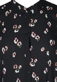 Svart blus med krage och knappslå, prydd med ett flerfärgat abstrakt mönster av rosa, grön och vita former.