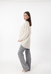 Maglione oversize beige chiaro con una maglia texture, abbinato a jeans a gamba larga grigio chiaro e sandali con cinturino. Sfondo bianco puro.