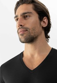 Černé tričko s výstřihem do V vyrobené z hladké látky, s přiléhavým střihem. Výstřih je nízký, s krátkými rukávy a minimálními švy.