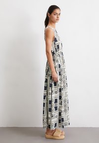 Maxi-jurk in een patroon van marineblauw en crème stof, met een aansluitende taille en een losse rok. G gedragen met lichtgekleurde, geweven platform sandalen.