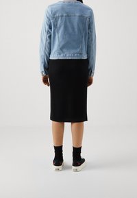 Person wearing a light blue denim jacket, black midi skirt, black socks, and black Converse sneakers with cherry designs, standing facing away.