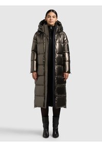 Duga jakna na punjenje u metalik tamno maslinastoj boji, s prošivenim dijelovima, kapuljačom i crnim patentnim zatvaračima. Nošena preko crne odjeće i čizama do koljena.