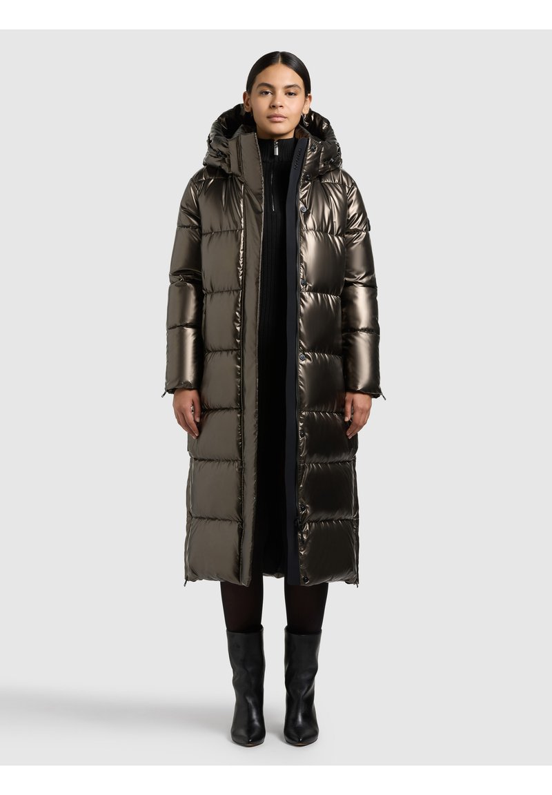 Duga jakna na punjenje u metalik tamno maslinastoj boji, s prošivenim dijelovima, kapuljačom i crnim patentnim zatvaračima. Nošena preko crne odjeće i čizama do koljena.