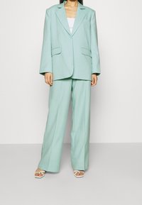 Blazer oversized verde menta e pantaloni a gamba larga abbinati in un tessuto morbido. Una maglietta bianca e sandali bianchi open toe completano l'outfit.