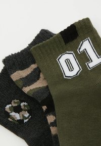 Set bestehend aus drei Socken: zwei in Dunkelgrau mit Pfotenabdruck und Camouflage-Muster und eine olivgrüne mit weißem "01"-Label. Stricktextur.