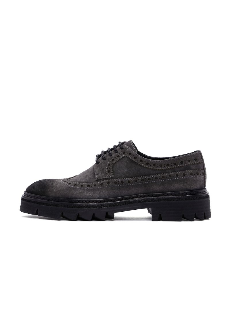 Chaussure en daim gris à lacets avec des détails de brogue, une épaisse semelle plateforme noire et une finition texturée. Le design allie des éléments classiques et modernes.