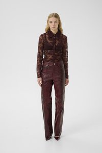 Bordeaux kanten blouse met lange mouwen, een puntkraag en knoopsluiting, gecombineerd met hoog uitgeknipte, donkerrode nep-krokodillenleren broek.