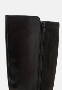 Svarta knähöga stövlar med en slät läderpanel och en texturerad mockaövre, med en sidaker för stängning.