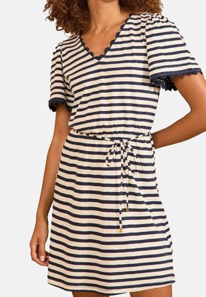Femme portant une robe à manches courtes rayée horizontalement noir et blanc avec des bords festonnés et une ceinture nouée à la taille.