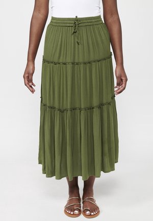 Person wearing a long olive green tiered skirt with drawstring waist and metallic strap sandals standing against a plain background.
