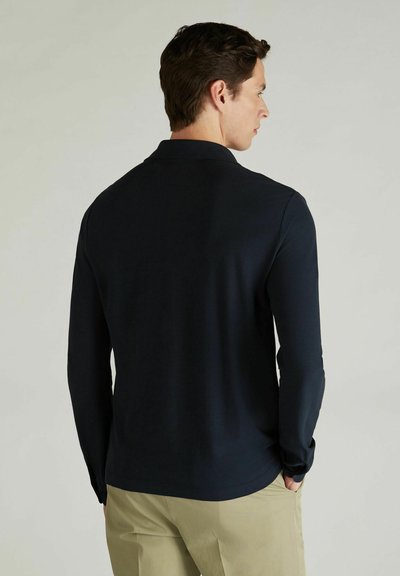 Polo à manches longues bleu marine avec un col ; texture lisse ; design ajusté. Associé à un pantalon beige clair, affichant un style décontracté.