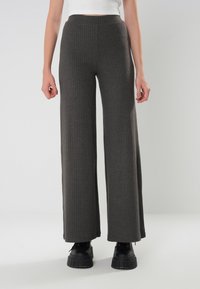 Breda byxor i ribbat tyg i mörkgrått med hög midja och texturerade detaljer, i kombination med svarta platåstövlar.