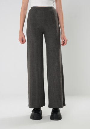 Pantaloni a gamba larga in tessuto grigio scuro con vita alta e dettagli testurizzati, abbinati a stivali platform neri.