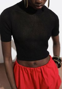 Zwarte geribbelde crop top met korte mouwen, gecombineerd met een rode rok met elastische taille. Gecombineerd met zwarte armbanden. Eenvoudig ontwerp, aansluitende stijl.
