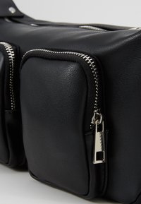 Borsa nera in pelle con due tasche con cerniera, forma rettangolare, superficie liscia e dettagli in metallo color argento.