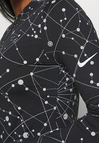 Schwarzes, sportliches Longsleeve-Oberteil mit einem silbernen, himmlischen Muster und Nike-Logo. Der Stoff ist glatt und hat eine taillierte Passform, die die Silhouette betont.