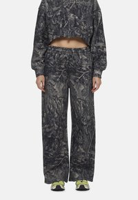 Kort sweatshirt en wijde broek in een donker camouflagepatroon. De stof lijkt zacht en heeft een elastische tailleband. Gdrag met groene sneakers.