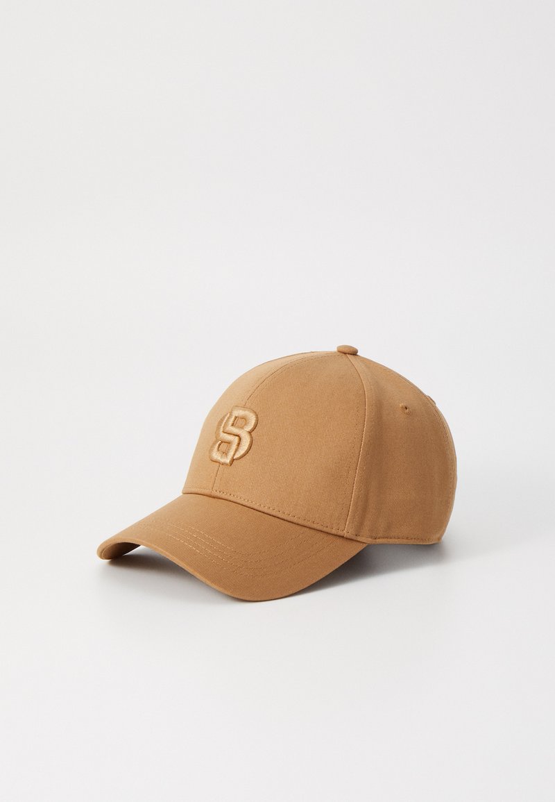 Tan baseball cap made of fabric with a curved visor. Features an embroidered logo on the front and ventilation eyelets on each side.