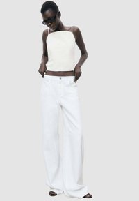 White wide-leg jeans with a high waist and front pockets paired with a fitted, square-neck, sleeveless white top.