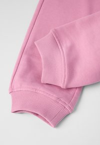 Lys rosa sweatshirtærme med ribbede manchetter og glat tekstur, der har synlige syningsdetaljer og en rund form ved kanten.