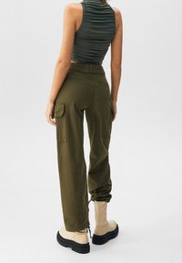 Pantaloni cargo verde oliva con tasche laterali e polsini elasticizzati, abbinati a stivali alla caviglia beige, realizzati in un tessuto resistente. Top strutturato non visibile.