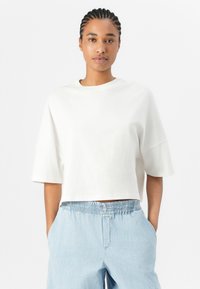 White cropped t-shirt made of cotton, featuring wide sleeves and a round neckline. Paired with light blue elastic-waist trousers.