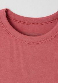 Maglietta a maniche corte con scollo rotondo, di colore rosa polveroso, realizzata in morbido cotone, con una texture a costine e dettagli di cucitura in vista.