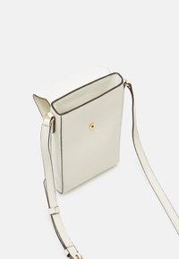 Liten strukturerad vit axelväska med klaffstängning, guldknapp och justerbar rem mot en enkel vit bakgrund.