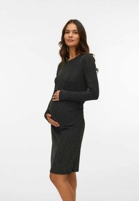 Zwangere jurk, lange mouwen, figuurvolgend ontwerp in zwart met subtiele zilveren glans. Zachte textuur, knie-lengte. Rimpel detail aan de voorkant.