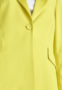 Yellow blazer with a single button closure, notch lapels, textured fabric, and side pocket. The design features clean, tailored lines.