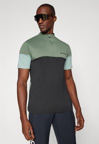 Polo de manga corta con cremallera en gris oscuro y verde claro, fabricado en material transpirable con mangas en contraste y logo de la marca en el pecho.