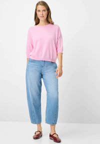 Pull à manches courtes rose clair associé à un jean ample bleu clair. Chaussures rouges avec des accents dorés. Tenue simple et décontractée.