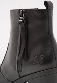 Bottine en cuir noir avec fermeture éclair latérale, languette à l'arrière, logo rond embossé sur le talon et semelle à talon bloc.