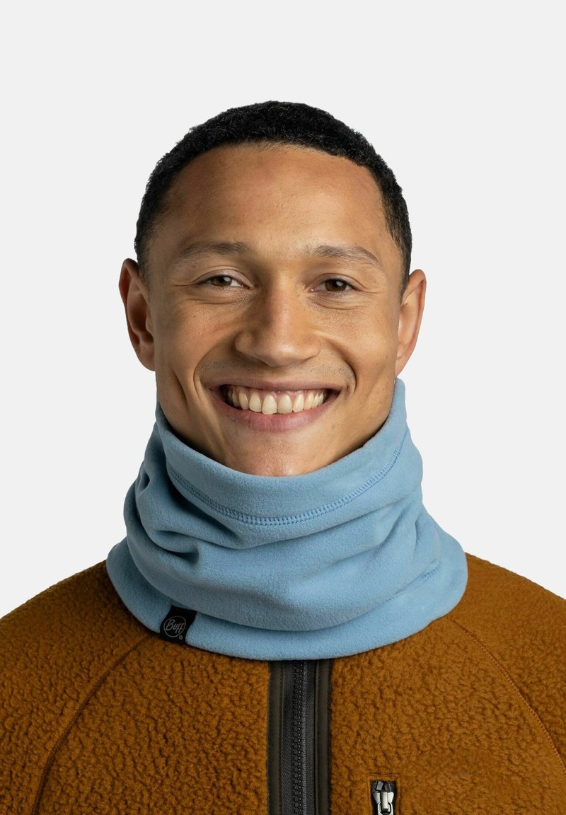 Gaiter de cuello de forro polar azul claro con una textura suave, que presenta un diseño sin costuras y una etiqueta de marca, llevado sobre una chaqueta de forro polar marrón.