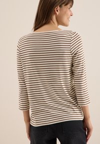 Haut à manches longues à rayures comportant de fines rayures marron et beige, avec un col rond et un tissu texturé, associé à un pantalon foncé.